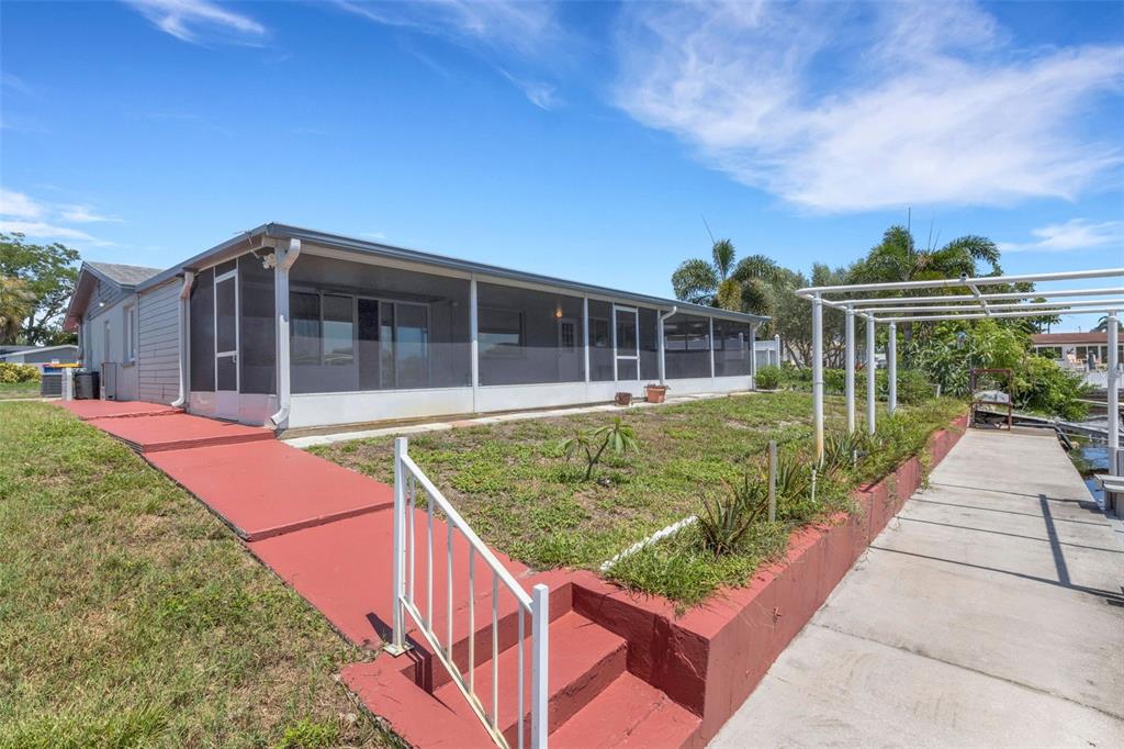 A house with a screened-in porch, a red walkway, and a concrete dock by water — 1240 TRUNKFISH DRIVE, HOLIDAY, FL