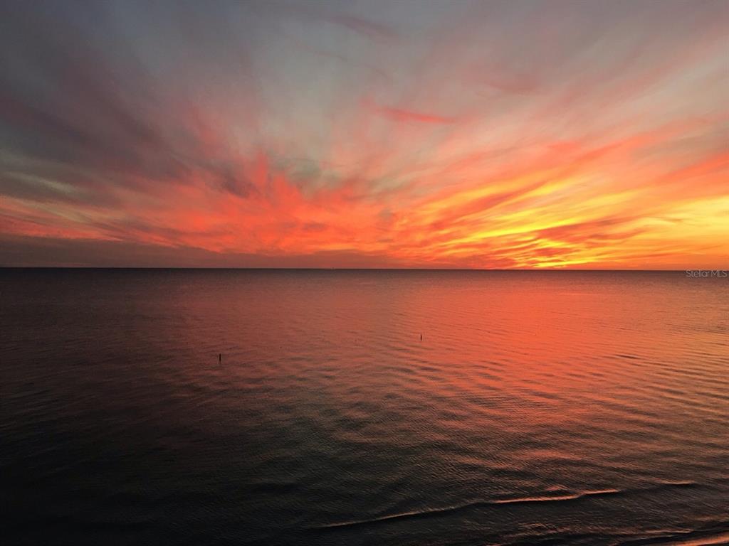 A vibrant orange and red sunset glows over a calm, dark ocean horizon — 100 BLUFF VIEW DRIVE UNIT 317A, BELLEAIR BLUFFS, FL