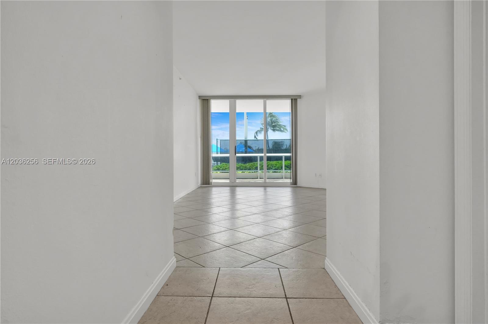 An empty room with light-colored tile flooring leads to a glass sliding door with balcony views — 4779 Collins Ave # 506, Miami Beach FL 33140, MIAMI BEACH, FL
