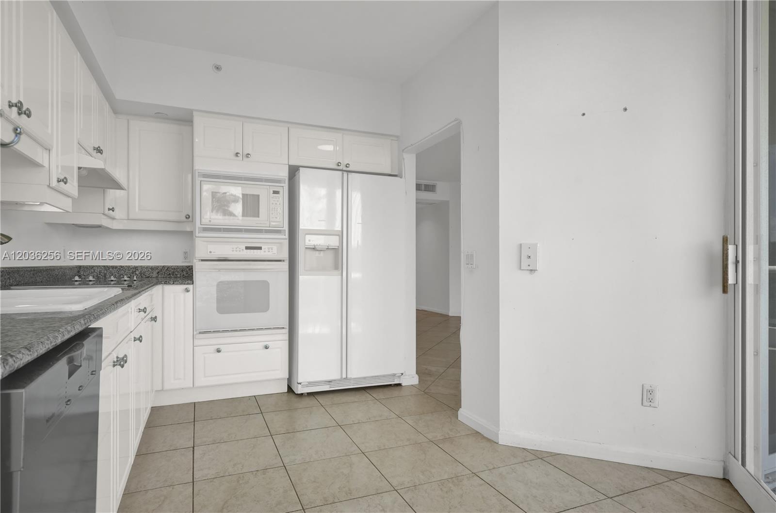 A white kitchen features tile flooring, granite countertops, and a built-in oven and microwave — 4779 Collins Ave # 506, Miami Beach FL 33140, MIAMI BEACH, FL