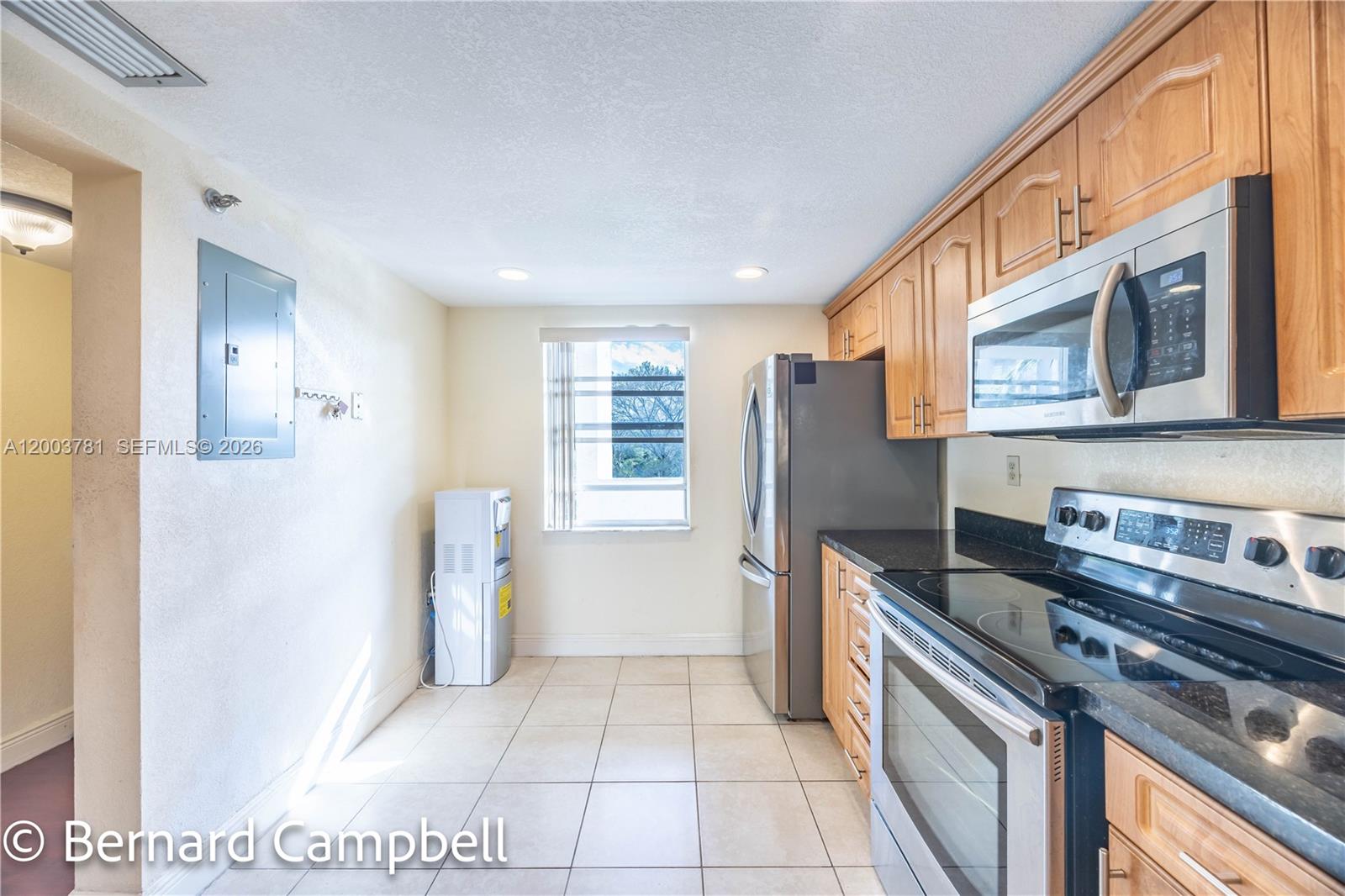A kitchen features light wood cabinets, stainless steel appliances, black countertops, and tile flooring — 3940 Inverrary Blvd # A, Lauderhill FL 33319, LAUDERHILL, FL