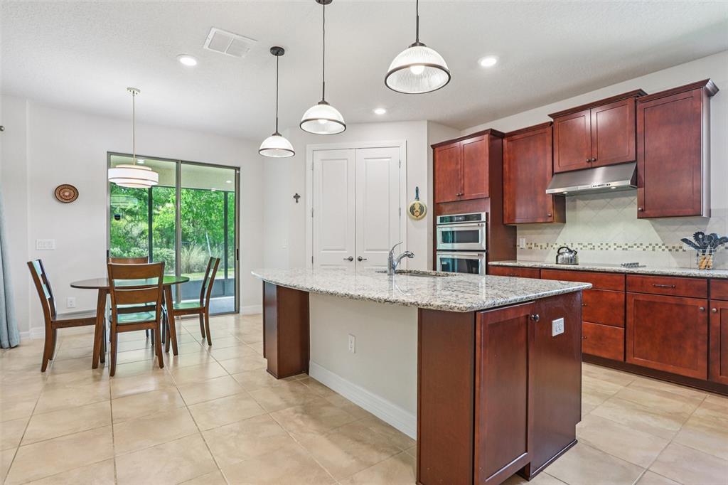 A kitchen with dark wood cabinets, a granite island, and an adjacent dining area — 19246 BRIARBROOK DRIVE, TAMPA, FL