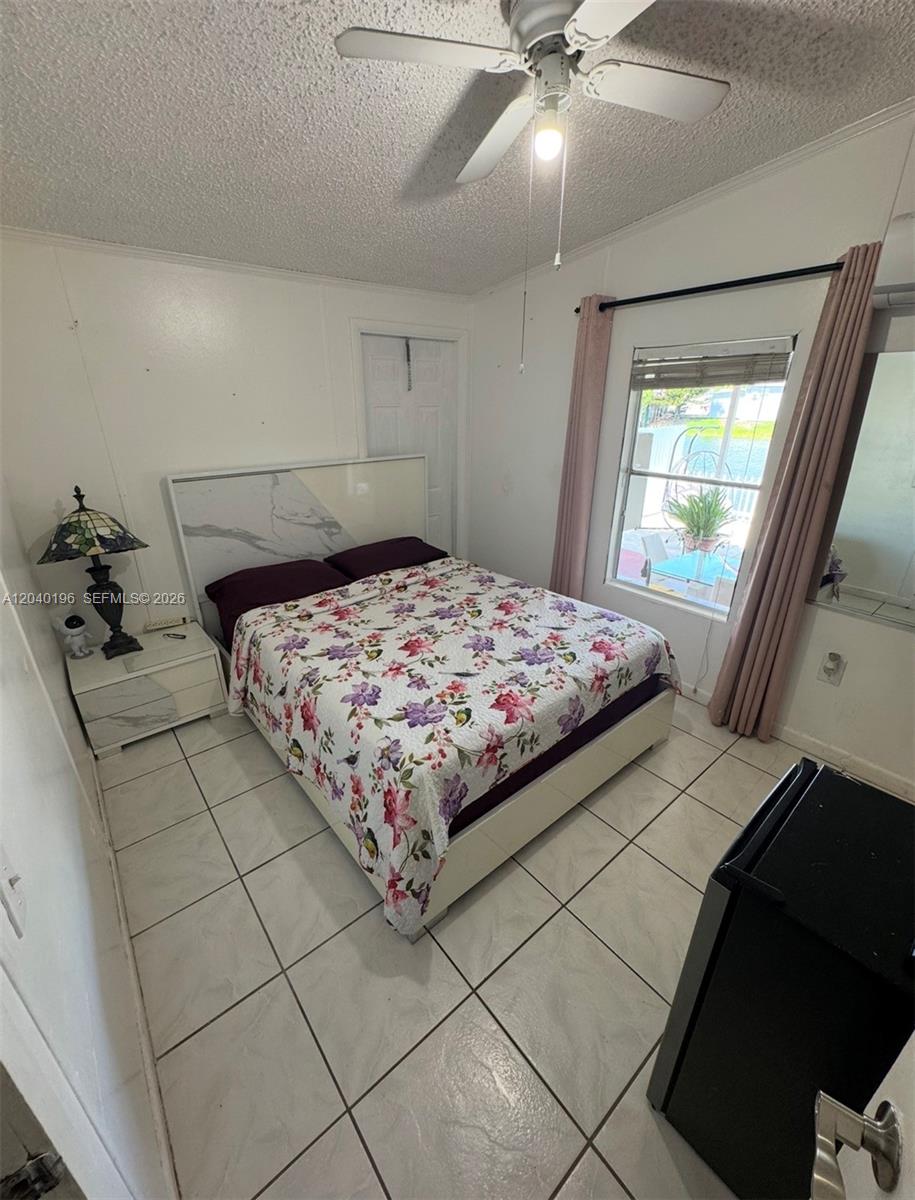A bedroom features a floral bedspread, white tile flooring, and a window with pink curtains — 1013 SW 128TH Ave, Miami FL 33184, MIAMI, FL