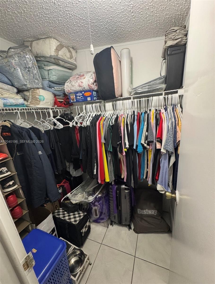 A walk-in closet features white wire shelving, hanging clothes, and various storage items — 1013 SW 128TH Ave, Miami FL 33184, MIAMI, FL
