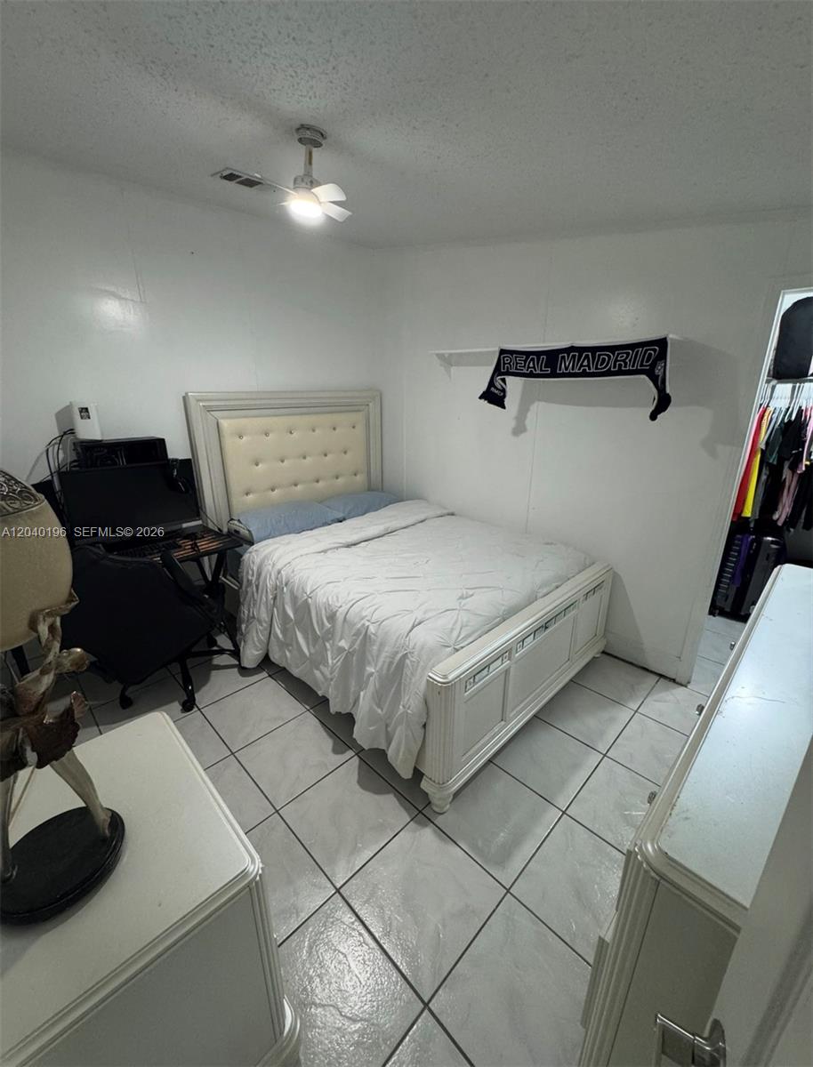 A bedroom features a white bed frame, tiled flooring, and a desk area — 1013 SW 128TH Ave, Miami FL 33184, MIAMI, FL
