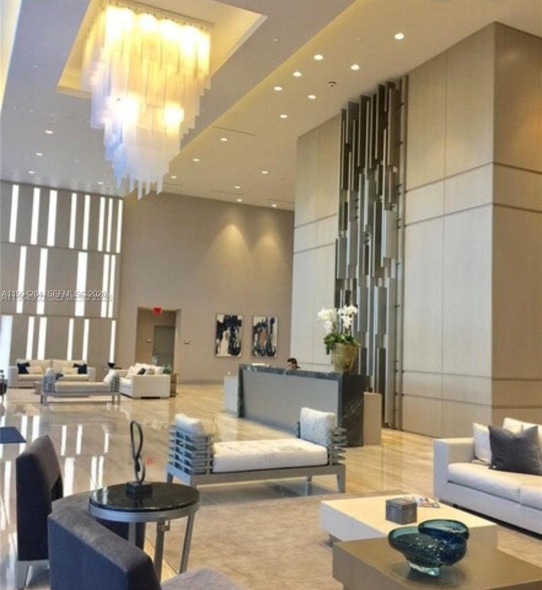 A spacious, modern lobby features a large tiered chandelier, marble floors, and contemporary seating areas — 5300 NW 85 # 1106, Doral FL 33166, DORAL, FL