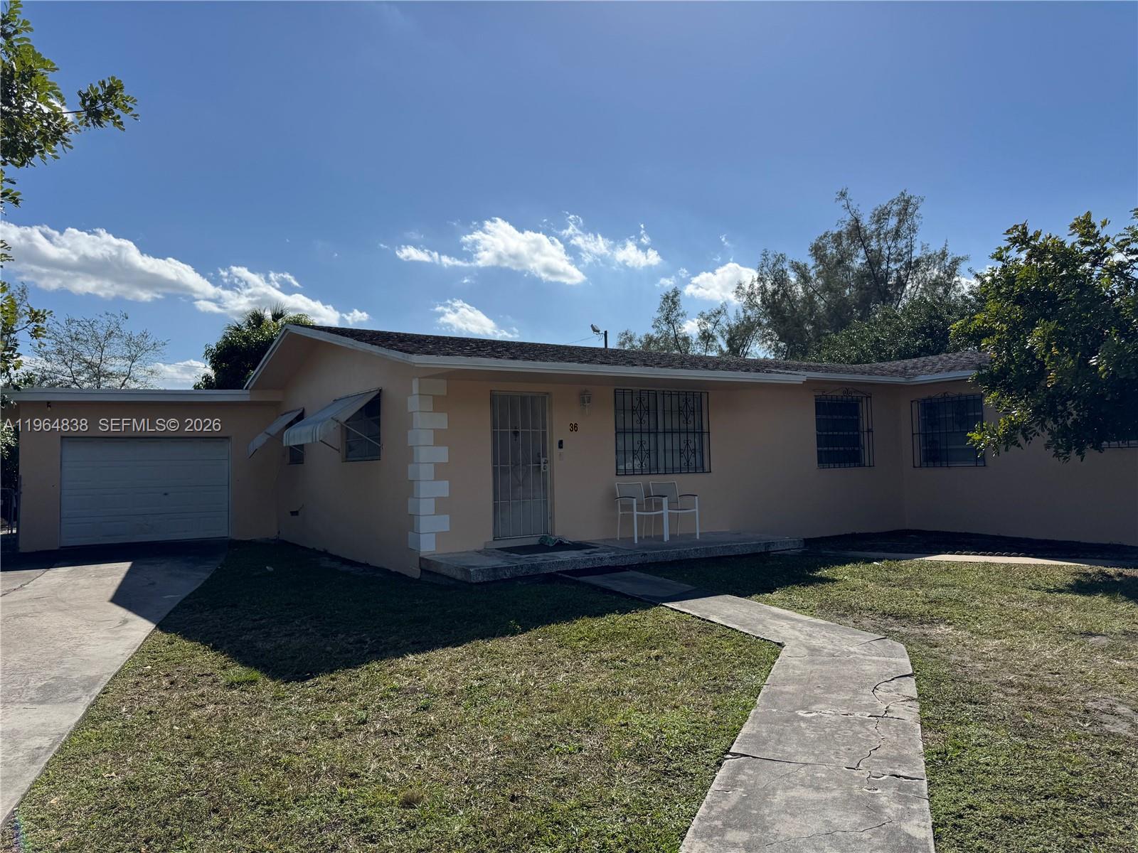 A single-story peach-colored house features a concrete driveway, a garage, and a front walkway — 36 NW 151st St, Miami FL 33169, MIAMI, FL