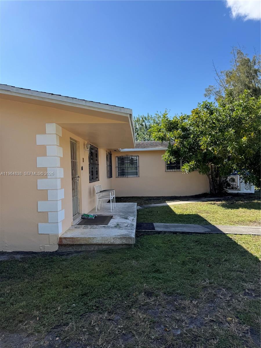 A peach-colored house exterior features a concrete porch, white corner accents, and metal window grilles — 36 NW 151st St, Miami FL 33169, MIAMI, FL