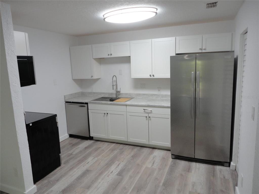 A kitchen features white cabinets, stainless steel appliances, a gray countertop, and wood-look flooring — 1015 SW 9TH STREET UNIT C-24, GAINESVILLE, FL