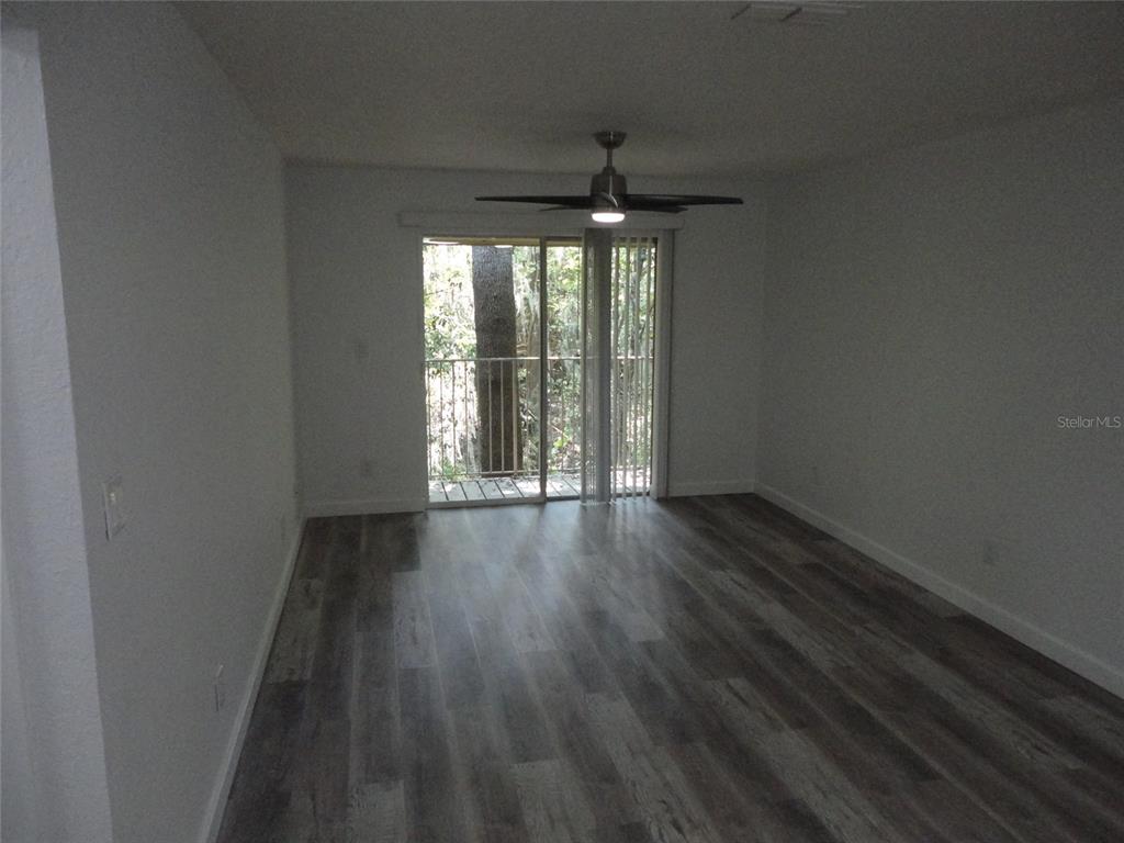 An empty room features wood-look flooring, a ceiling fan, and a sliding glass door — 1015 SW 9TH STREET UNIT C-24, GAINESVILLE, FL
