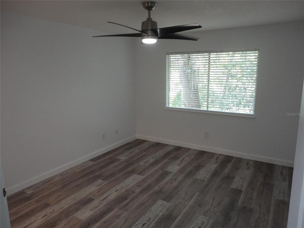An empty bedroom features white walls, wood-look flooring, a ceiling fan, and a window — 1015 SW 9TH STREET UNIT C-24, GAINESVILLE, FL