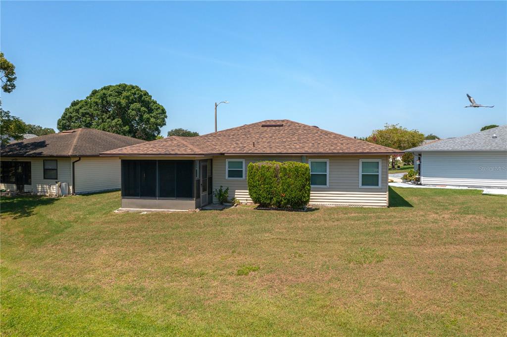 The rear exterior of a single-story house features a screened-in porch and tan siding — 3245 PRAIRIE DUNES CIRCLE E, LAKELAND, FL