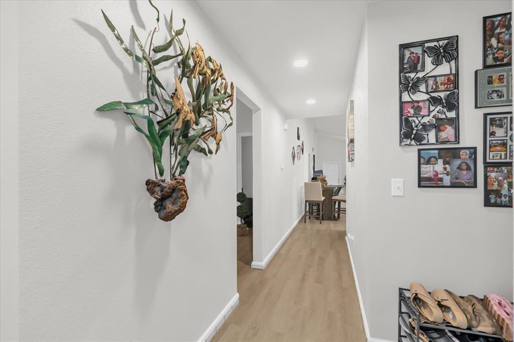 A hallway with light wood flooring, wall art, and a view into a dining area — 119 D STREET, LAKE WALES, FL