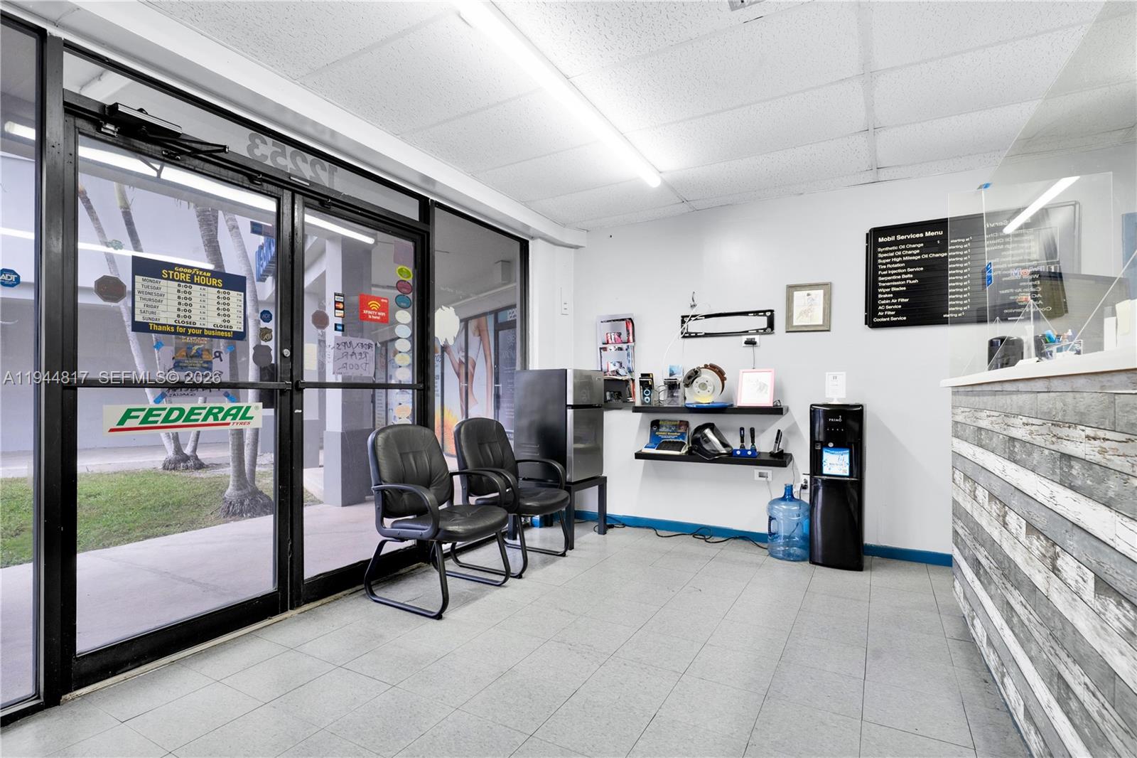 A waiting area in an auto shop features two black chairs, a water cooler, and signage — 12225 SW 112th St, Miami FL 33186, MIAMI, FL