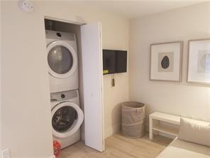 A room features a stacked washer and dryer unit, a wall-mounted television, and a laundry hamper — 16385 Biscayne Boulevard # 1018, North Miami Beach FL 33160, NORTH MIAMI BEACH, FL
