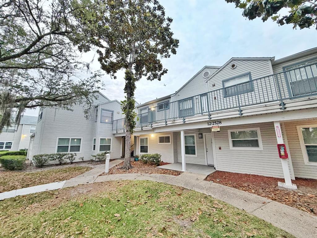 A two-story apartment building with light-colored siding, a metal balcony, and a paved walkway — 2528 WOODGATE BOULEVARD UNIT 102, ORLANDO, FL
