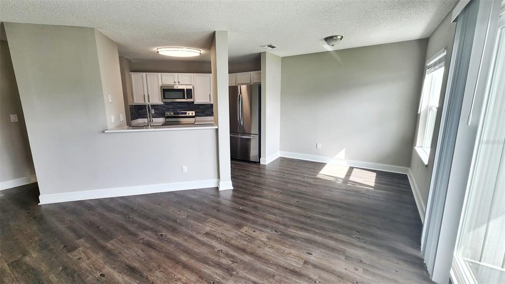 An open-concept kitchen with stainless steel appliances overlooks a living area with wood-look flooring — 2528 WOODGATE BOULEVARD UNIT 102, ORLANDO, FL