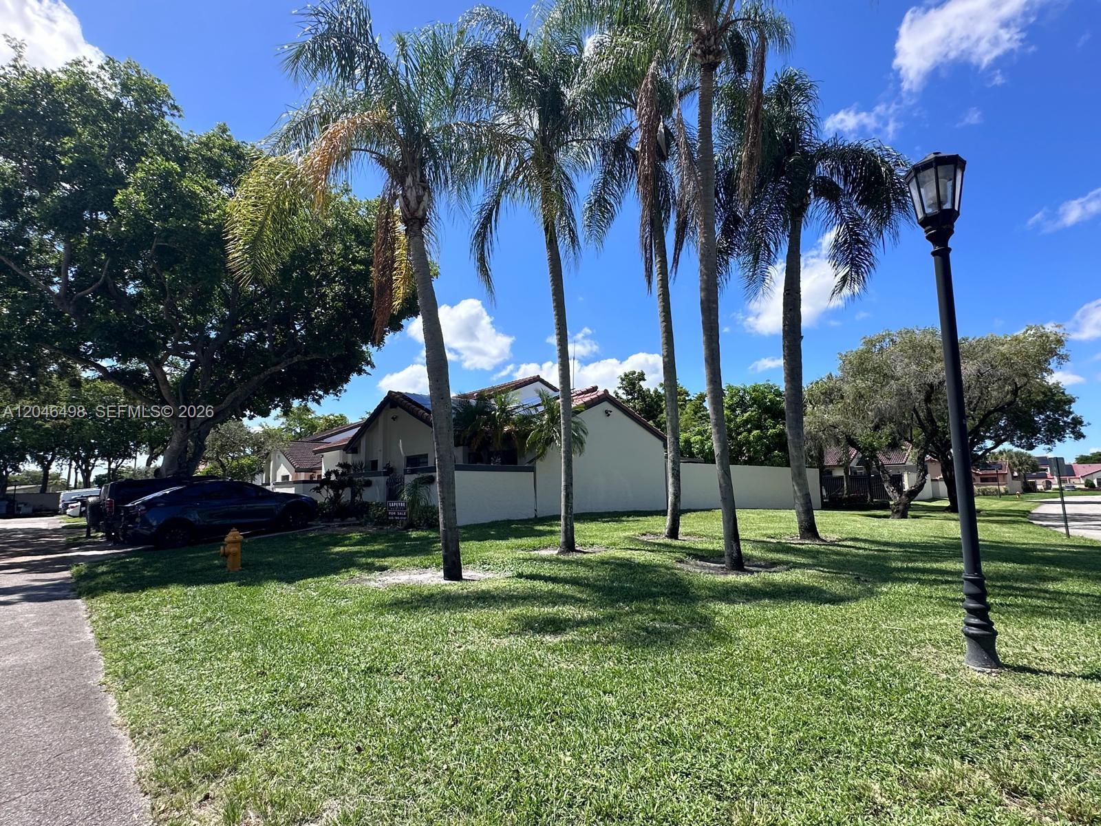 A single-story house with a white wall and palm trees sits on a grassy lawn — 6633 NW 178th Ter, Hialeah FL 33015, HIALEAH, FL