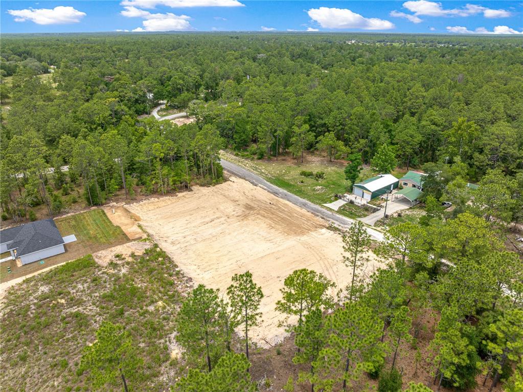 An aerial view shows a cleared, sandy residential lot surrounded by trees and neighboring houses — SW 38TH PLACE, OCALA, FL