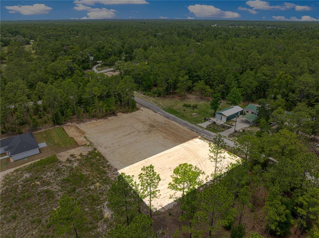An aerial view shows a cleared, rectangular residential lot surrounded by trees and nearby houses — SW 38TH PLACE, OCALA, FL