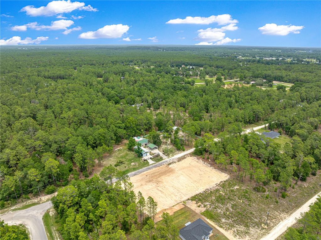 An aerial view shows a cleared, sandy residential lot surrounded by dense forest and nearby houses — SW 38TH PLACE, OCALA, FL