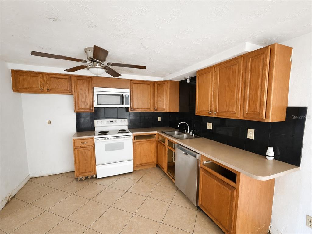 A kitchen with oak cabinets, white appliances, black tile backsplash, and light-colored tile flooring — 3303 EISENHOWER DRIVE, HOLIDAY, FL