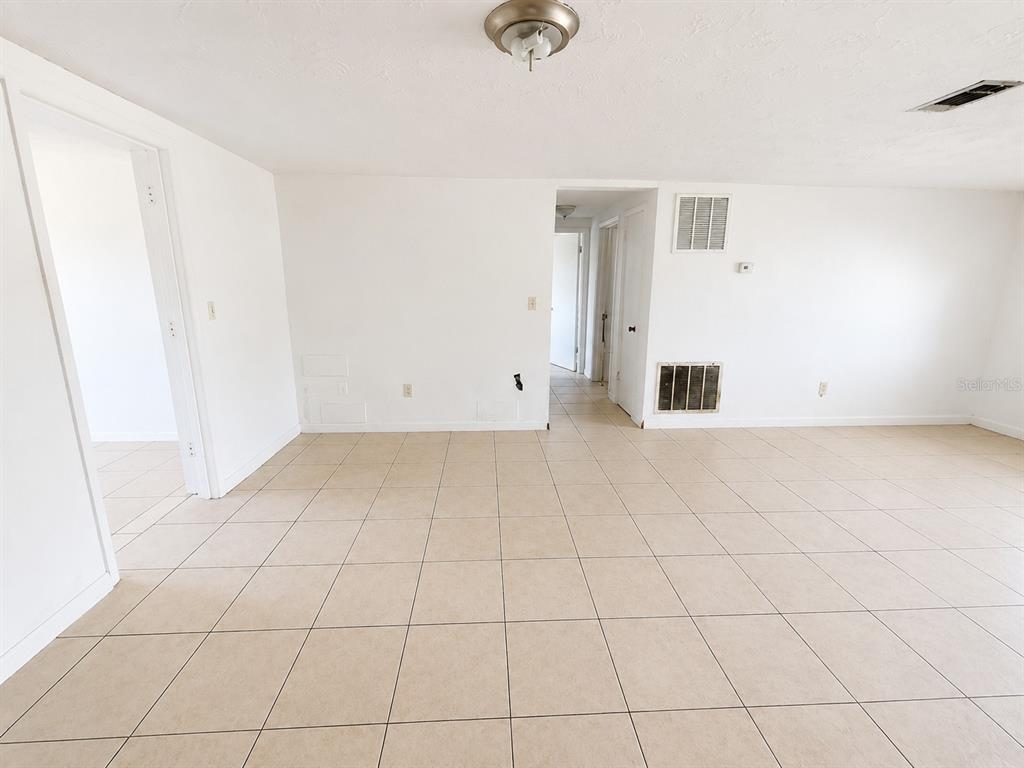 An empty room with white walls, beige tile flooring, and two doorways leading to hallways — 3303 EISENHOWER DRIVE, HOLIDAY, FL