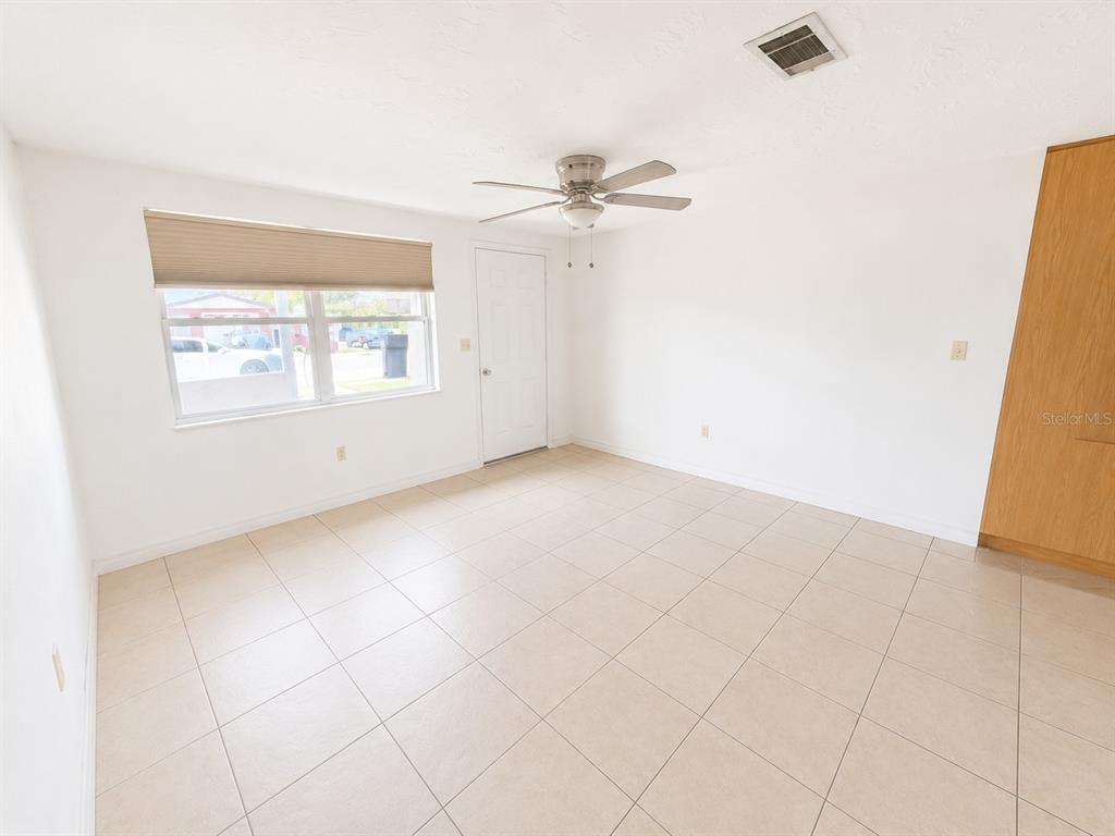 An empty room features white walls, light-colored tile flooring, a ceiling fan, and a window — 3303 EISENHOWER DRIVE, HOLIDAY, FL