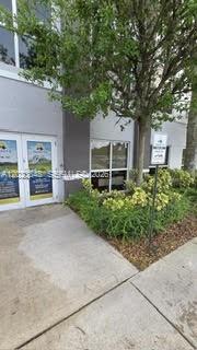 A concrete walkway leads to the glass-paned entrance of a multi-story building with landscaping — 12001 SW 128th Ct # 101, Miami FL 33186, MIAMI, FL