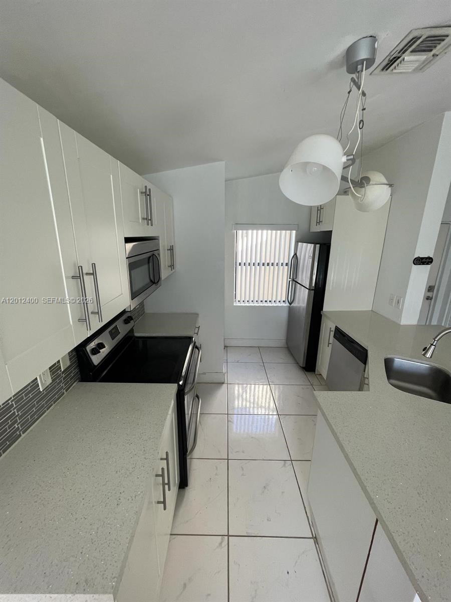 A galley-style kitchen features white cabinets, light countertops, stainless steel appliances, and tiled flooring — 9999 Summerbreeze Dr # 212, Sunrise FL 33322, SUNRISE, FL