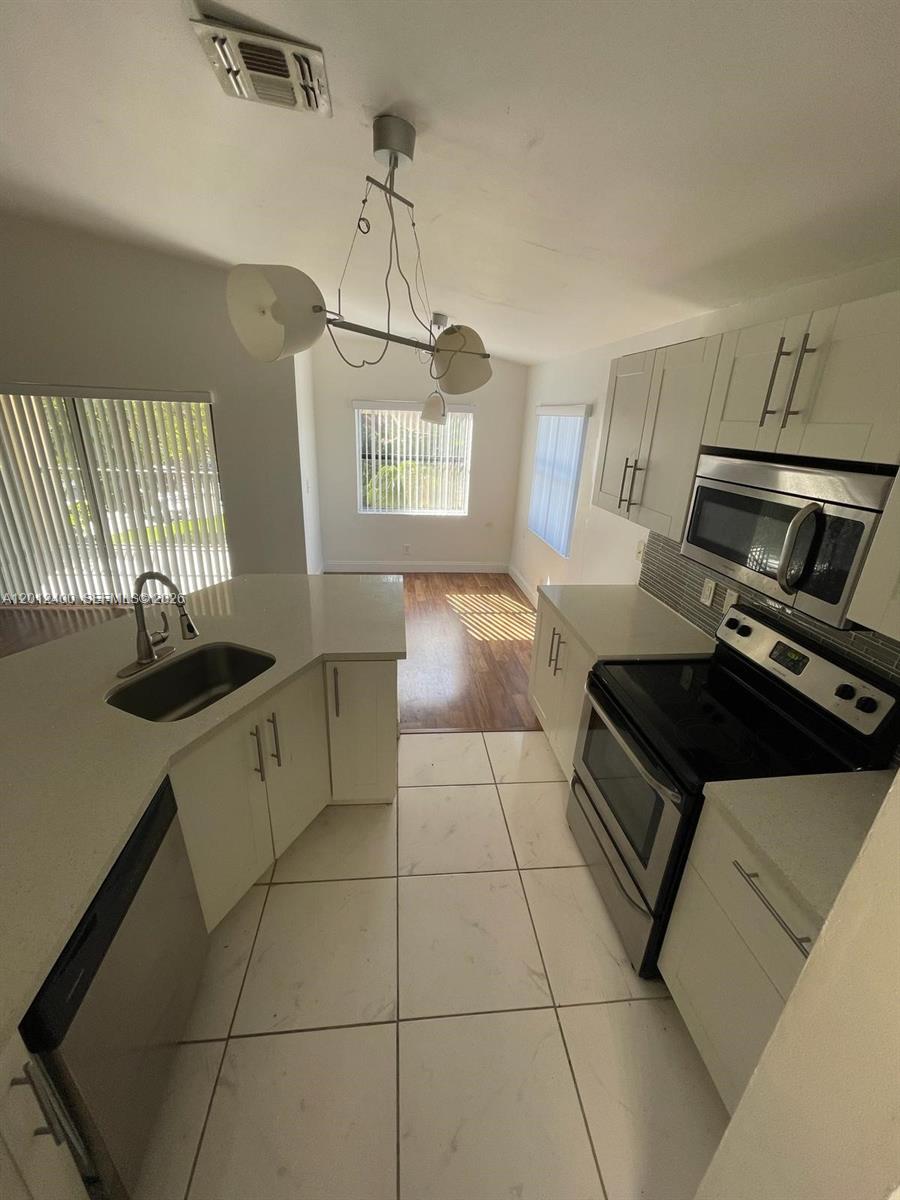 A kitchen features white cabinets, stainless steel appliances, and light-colored tile flooring — 9999 Summerbreeze Dr # 212, Sunrise FL 33322, SUNRISE, FL