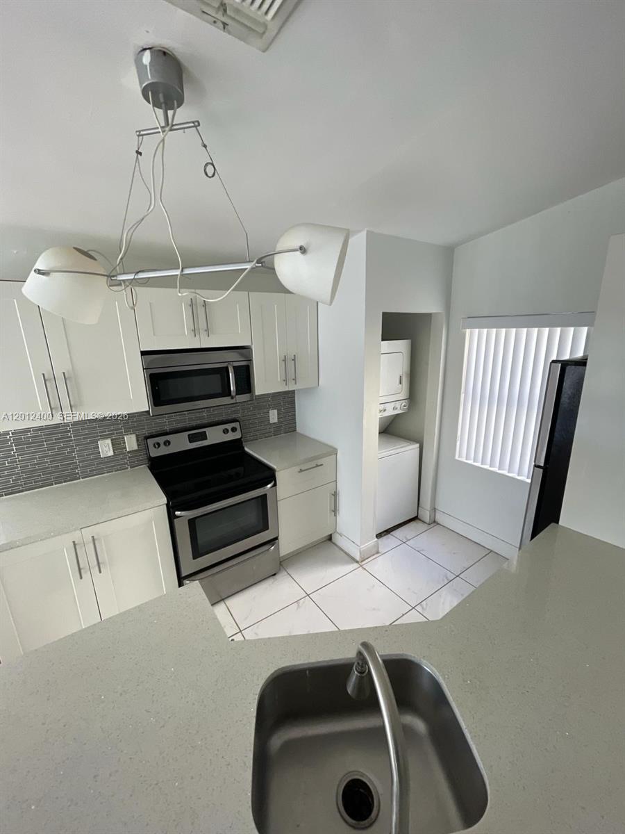 A kitchen features white cabinets, stainless steel appliances, a tiled backsplash, and a laundry closet — 9999 Summerbreeze Dr # 212, Sunrise FL 33322, SUNRISE, FL