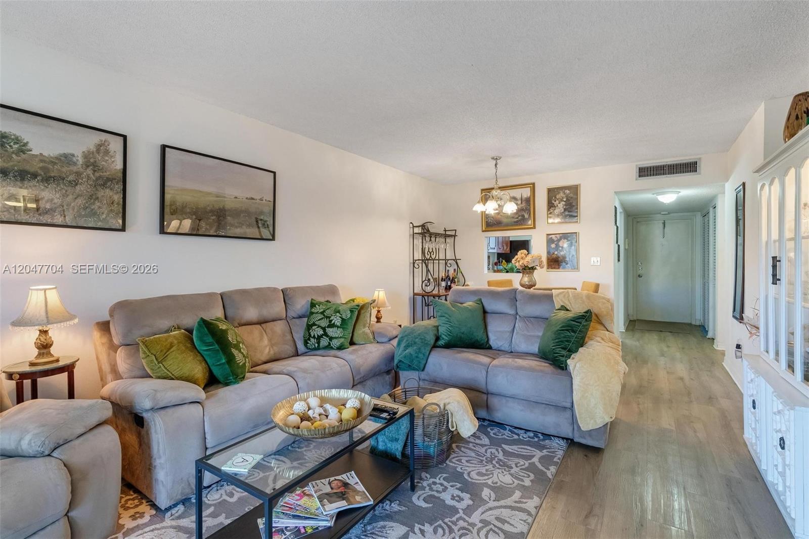 A living room features gray sofas, a glass coffee table, and light wood-look flooring — 6000 NW 64th Ave # 110, Tamarac FL 33319, TAMARAC, FL