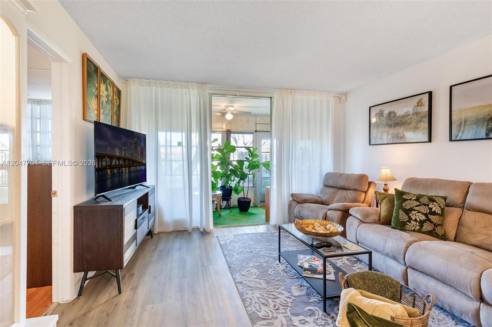A living room features light wood flooring, a gray sofa, and a glass-topped coffee table — 6000 NW 64th Ave # 110, Tamarac FL 33319, TAMARAC, FL