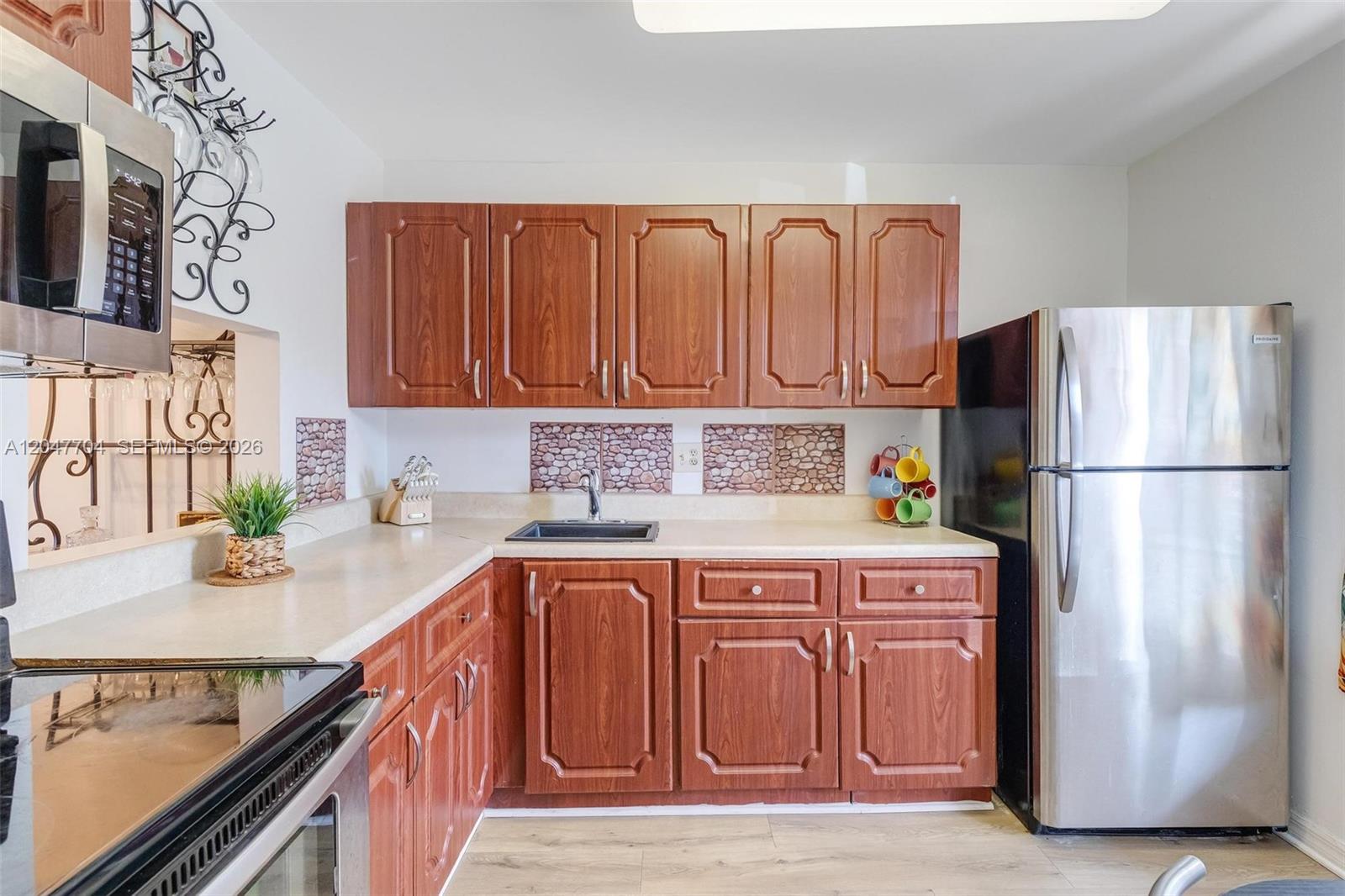A kitchen features wood cabinets, stainless steel appliances, and a stone-look tile backsplash — 6000 NW 64th Ave # 110, Tamarac FL 33319, TAMARAC, FL