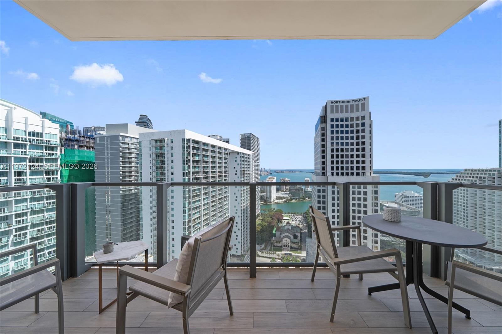 A high-rise balcony features outdoor furniture overlooking a city skyline and the ocean — 68 SE 6th St # 3209, Miami FL 33131, MIAMI, FL