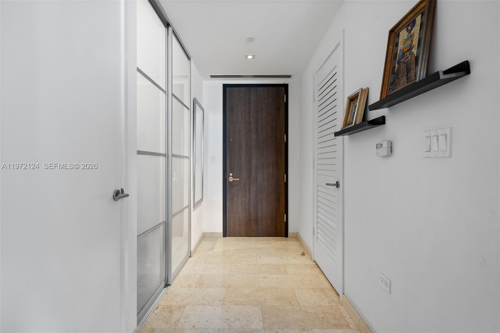 A hallway features a dark wood door, tiled flooring, and white walls with wall shelves — 68 SE 6th St # 3209, Miami FL 33131, MIAMI, FL