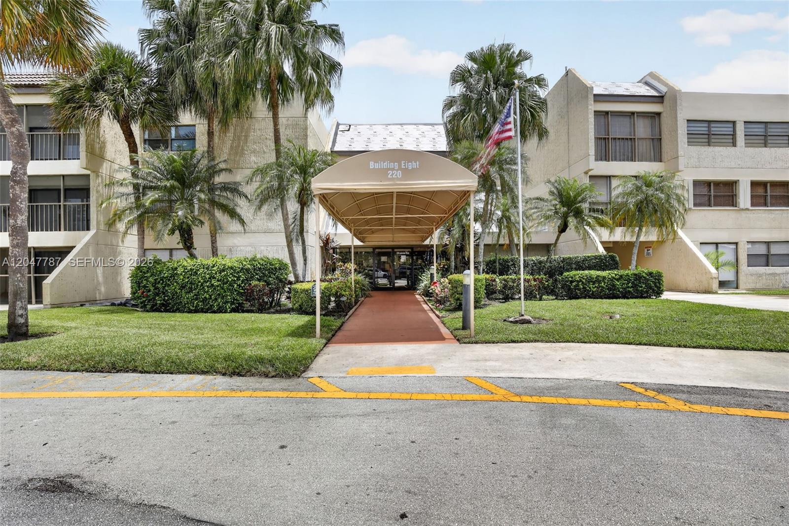 The exterior of a multi-story apartment building features a covered walkway and palm trees — 220 Lakeview Dr # 210, Weston FL 33326, WESTON, FL