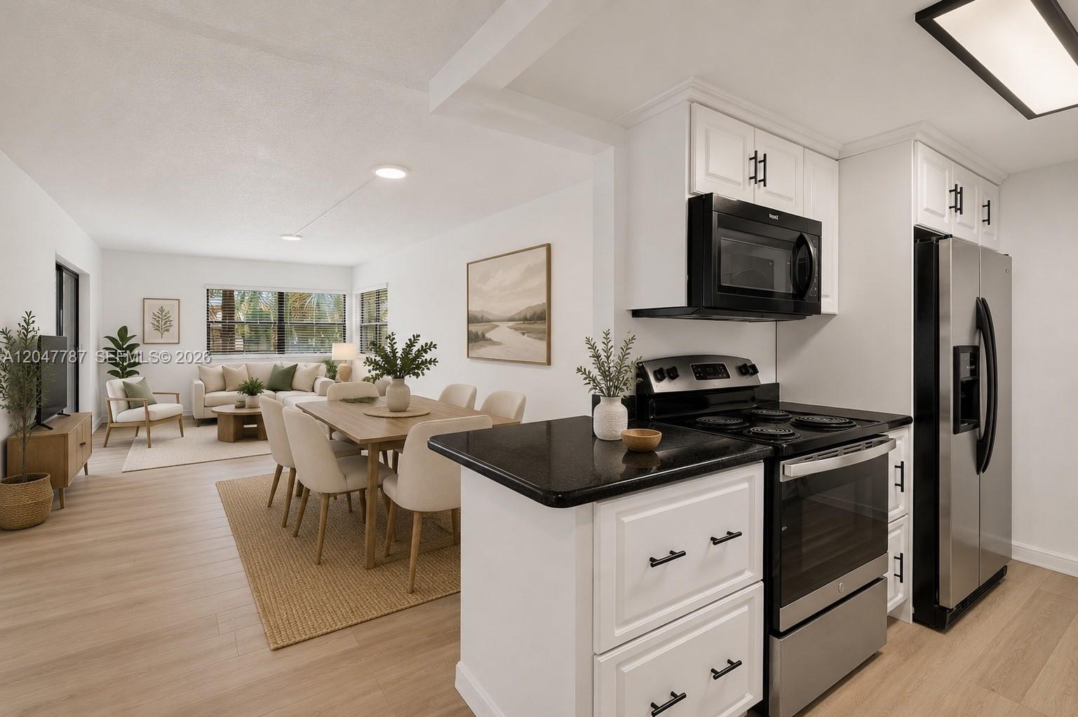 A kitchen with black appliances and white cabinets overlooks an open-concept dining and living area — 220 Lakeview Dr # 210, Weston FL 33326, WESTON, FL