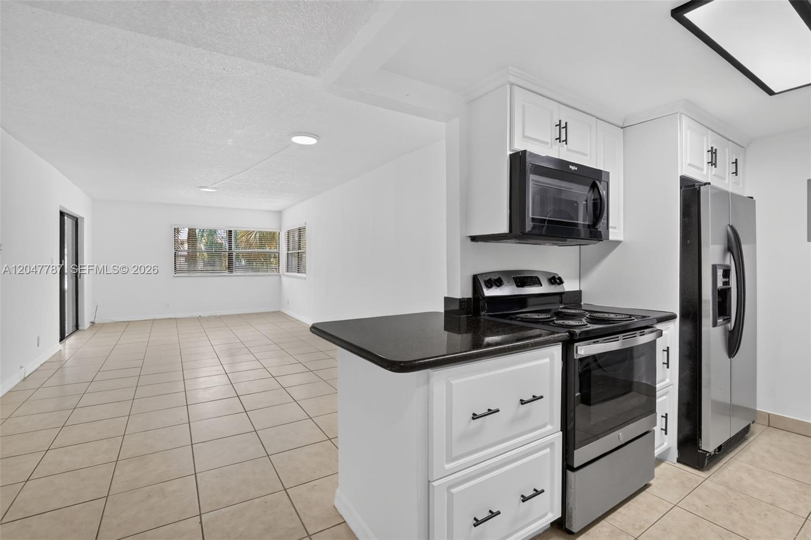 A kitchen with white cabinets and stainless steel appliances opens into a tiled living area — 220 Lakeview Dr # 210, Weston FL 33326, WESTON, FL