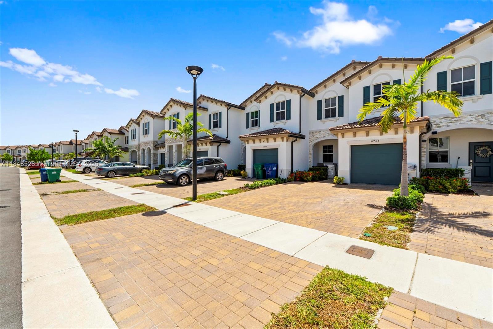 A row of two-story townhouses with paved driveways and attached garages under a blue sky — 12625 NW 23rd Pl, Miami FL 33167, MIAMI, FL