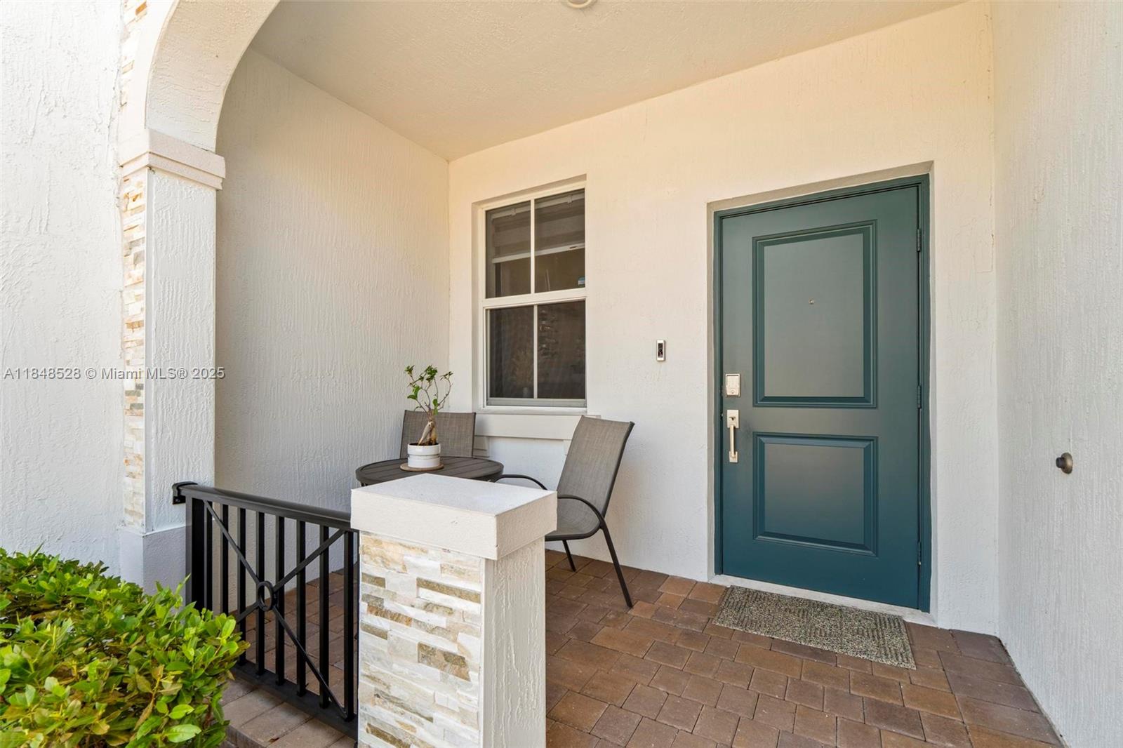 A covered front porch features a teal door, a small table with chairs, and pavers — 12625 NW 23rd Pl, Miami FL 33167, MIAMI, FL