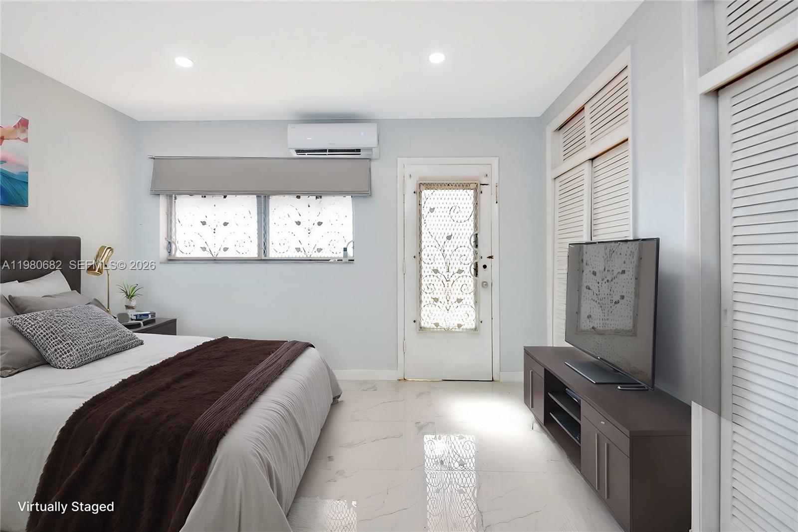 A bedroom features a bed, a television on a console, and a door with glass — 820 SW 11th Ave # 14B, Hallandale Beach FL 33009, HALLANDALE BEACH, FL