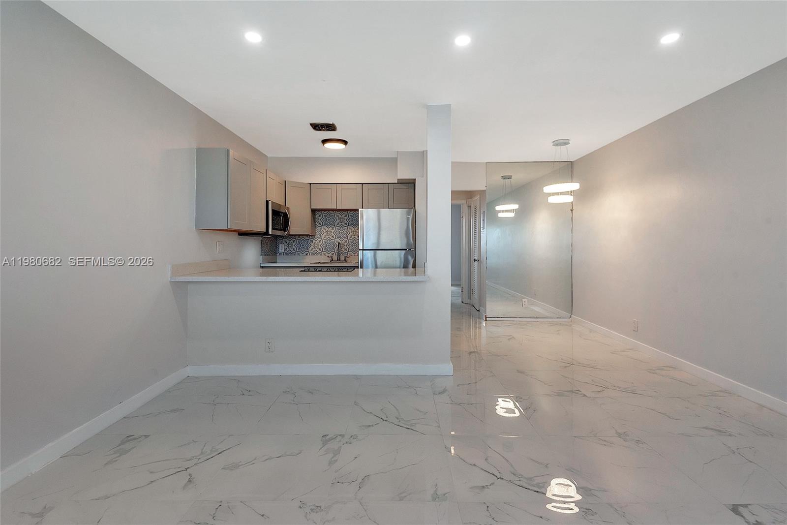 A kitchen with light cabinets and a patterned backsplash overlooks a dining area with mirrored walls — 820 SW 11th Ave # 14B, Hallandale Beach FL 33009, HALLANDALE BEACH, FL