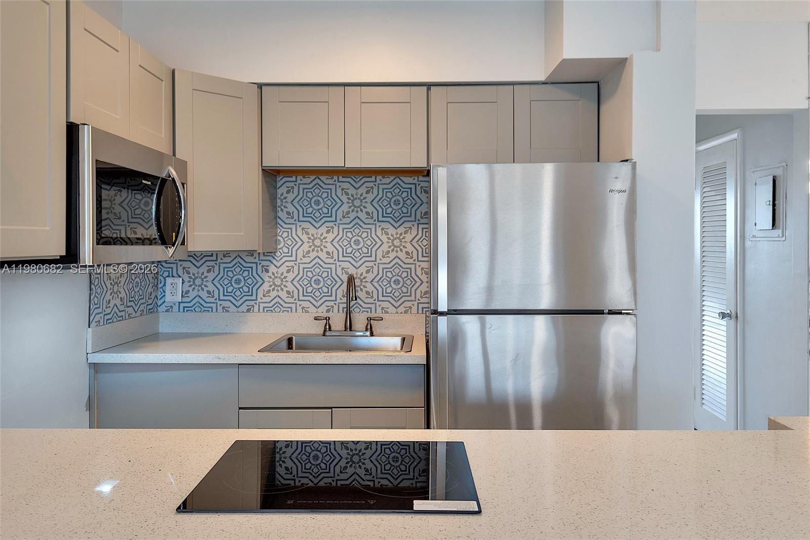 A kitchen features gray cabinets, a patterned tile backsplash, stainless steel appliances, and quartz countertops — 820 SW 11th Ave # 14B, Hallandale Beach FL 33009, HALLANDALE BEACH, FL