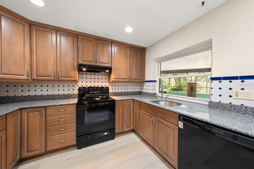 A kitchen features wood cabinets, granite countertops, a black stove, and a window over the sink — 3408 CULLENDALE DRIVE, TAMPA, FL