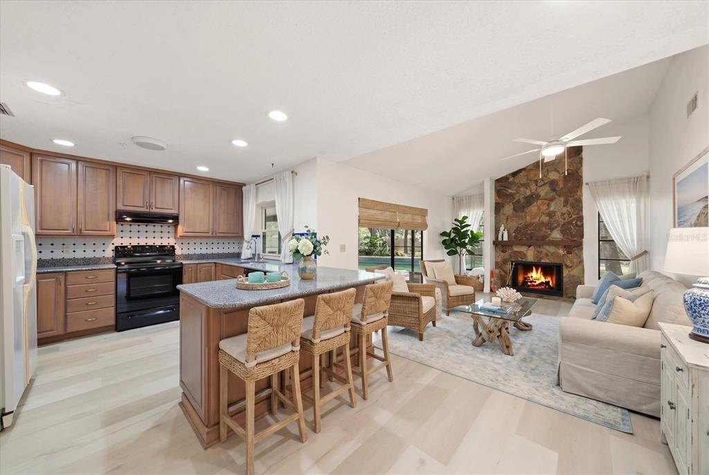 An open-concept kitchen and living room featuring wood cabinets, a stone fireplace, and light flooring — 3408 CULLENDALE DRIVE, TAMPA, FL