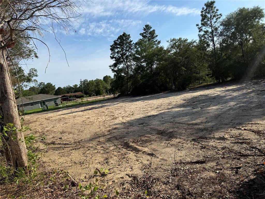 A cleared, sandy residential lot is surrounded by trees with a house in the distance — 00 SW MARINE BOULEVARD, DUNNELLON, FL