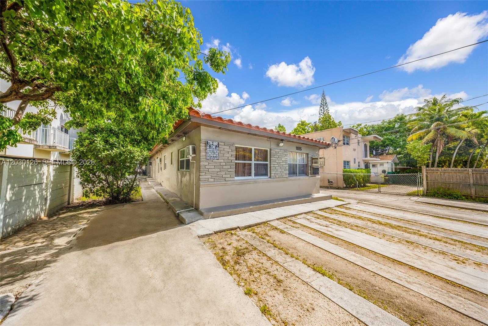 A single-story house with a stone facade and a tiled roof sits beside a driveway — 1035 NW 4th St, Miami FL 33128, MIAMI, FL