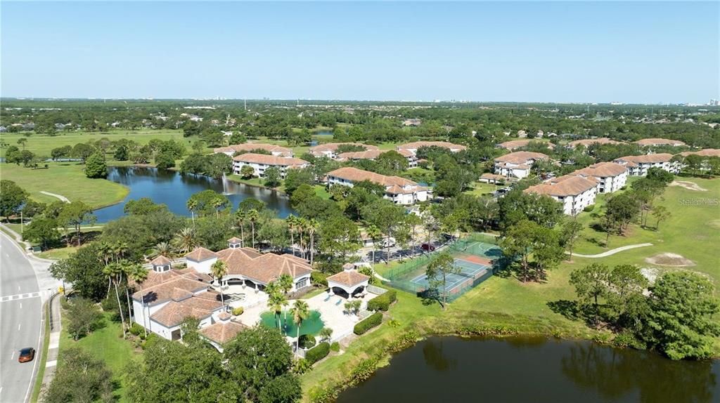 An aerial view shows a residential complex with a pool, tennis court, and surrounding lakes — 14049 FAIRWAY ISLAND DRIVE UNIT 127, ORLANDO, FL